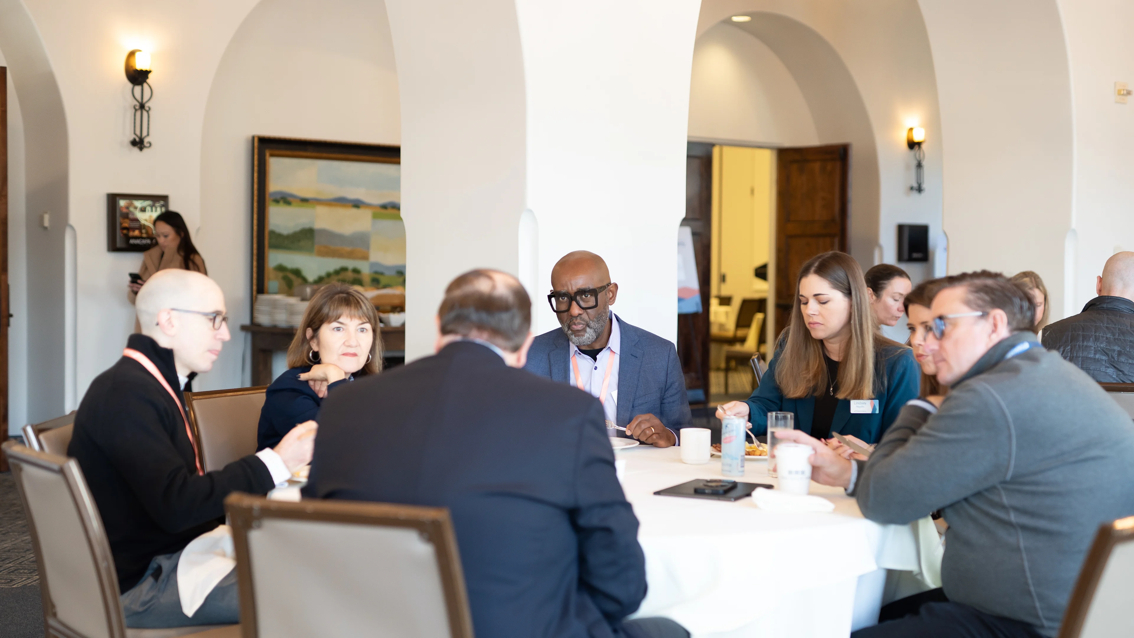 A group of professionals seated around a round table engaged in conversation during a formal meeting or event. 