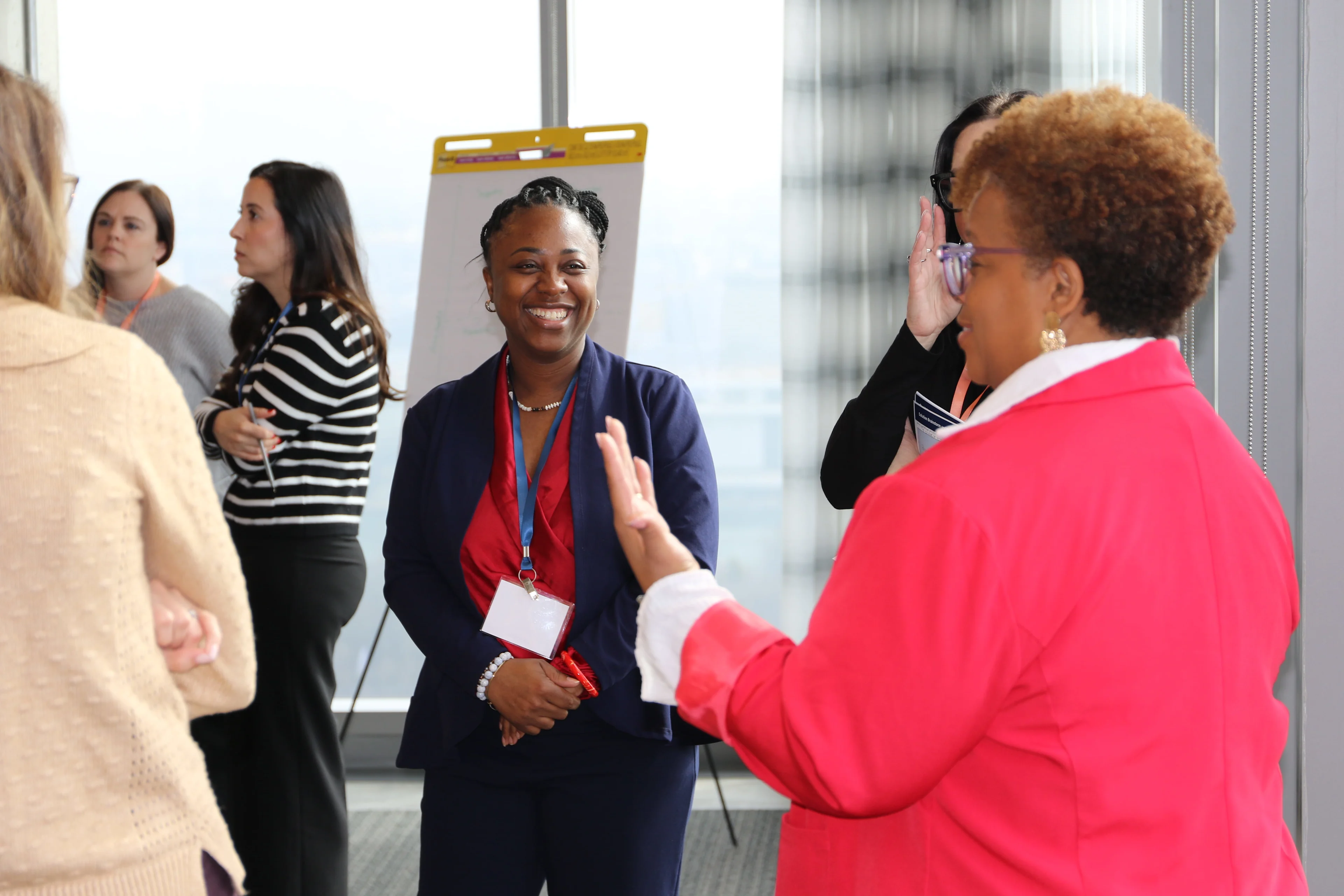 A group of nurse managers in business attire standing in a brightly lit room, engaged in a lively conversation during a networking event
