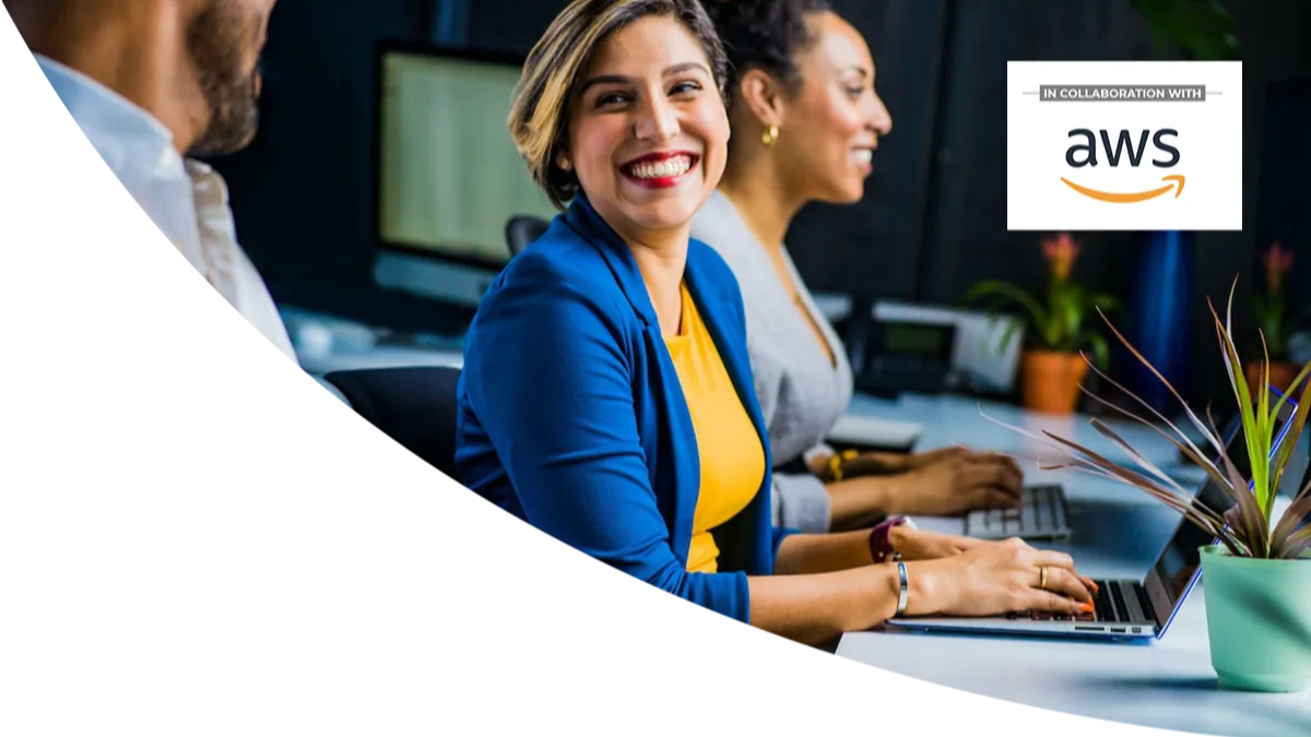 Woman in a blue blazer smiling at her desk, working alongside colleagues in a modern office setting, with an AWS collaboration logo displayed in the background.