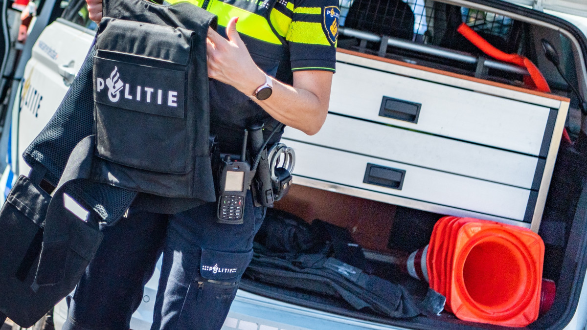 Een politieagent die een kogelwerend vest uit de achterbak van een auto haalt