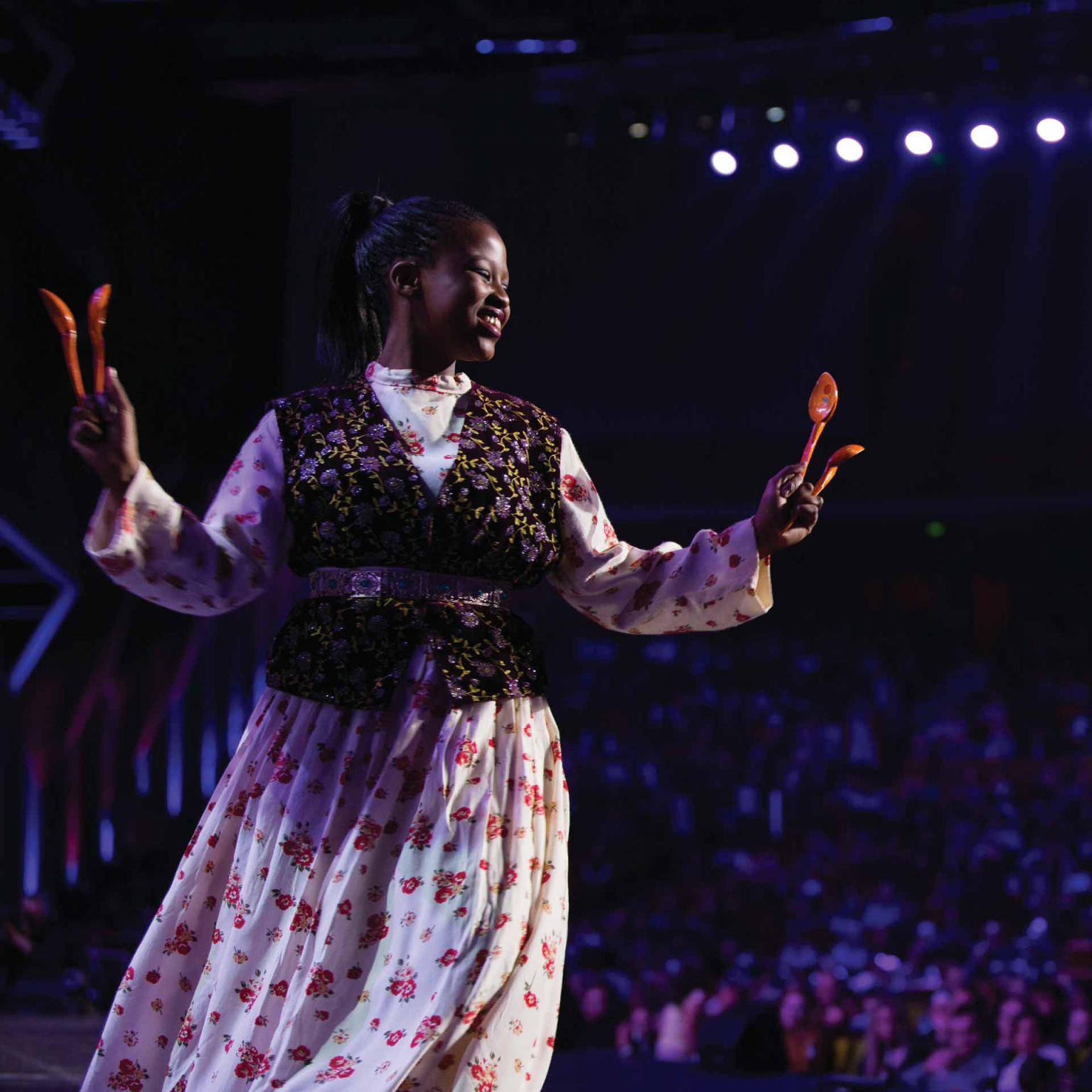 Woman in a floral dress on stage dancing with her hands up in the air. 