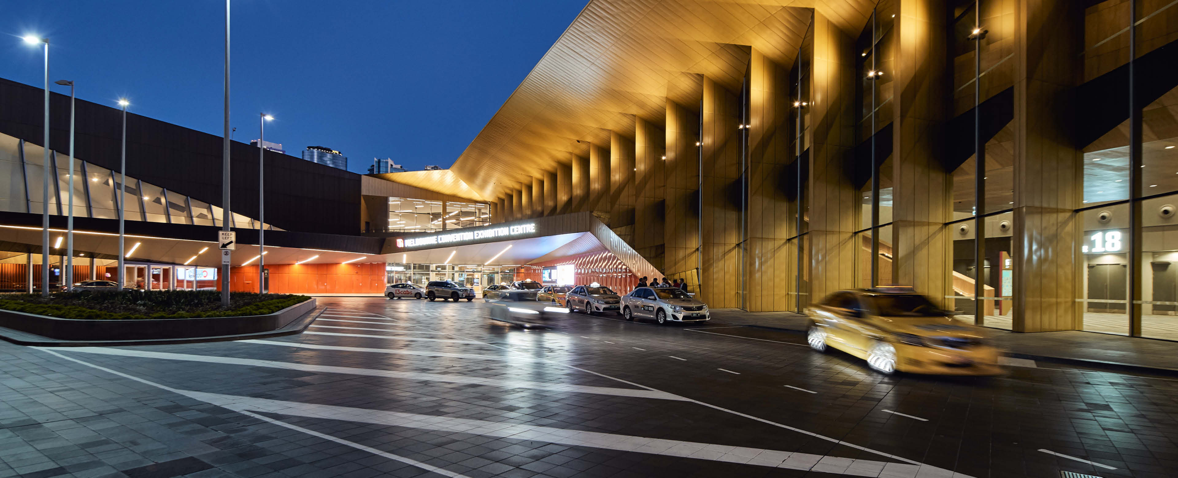 One side of the Melbourne Convention and Exhibition Centre, featuring a row of parked cars in front of a striking golden wall, with the night sky overhead.