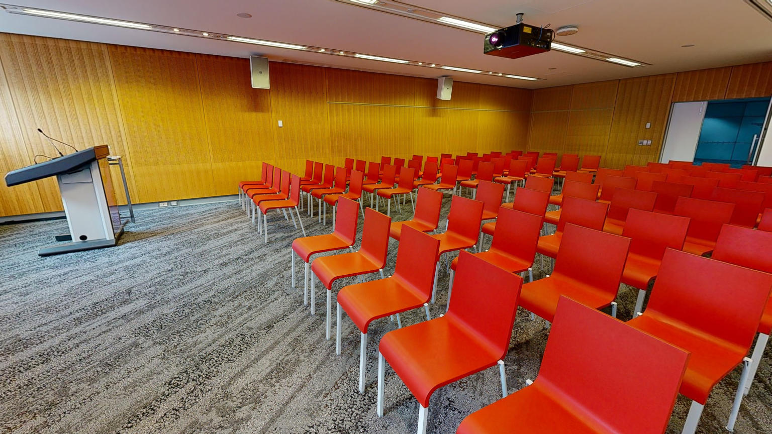 Conference or meeting room with orange chairs set up in rows facing a lectern.