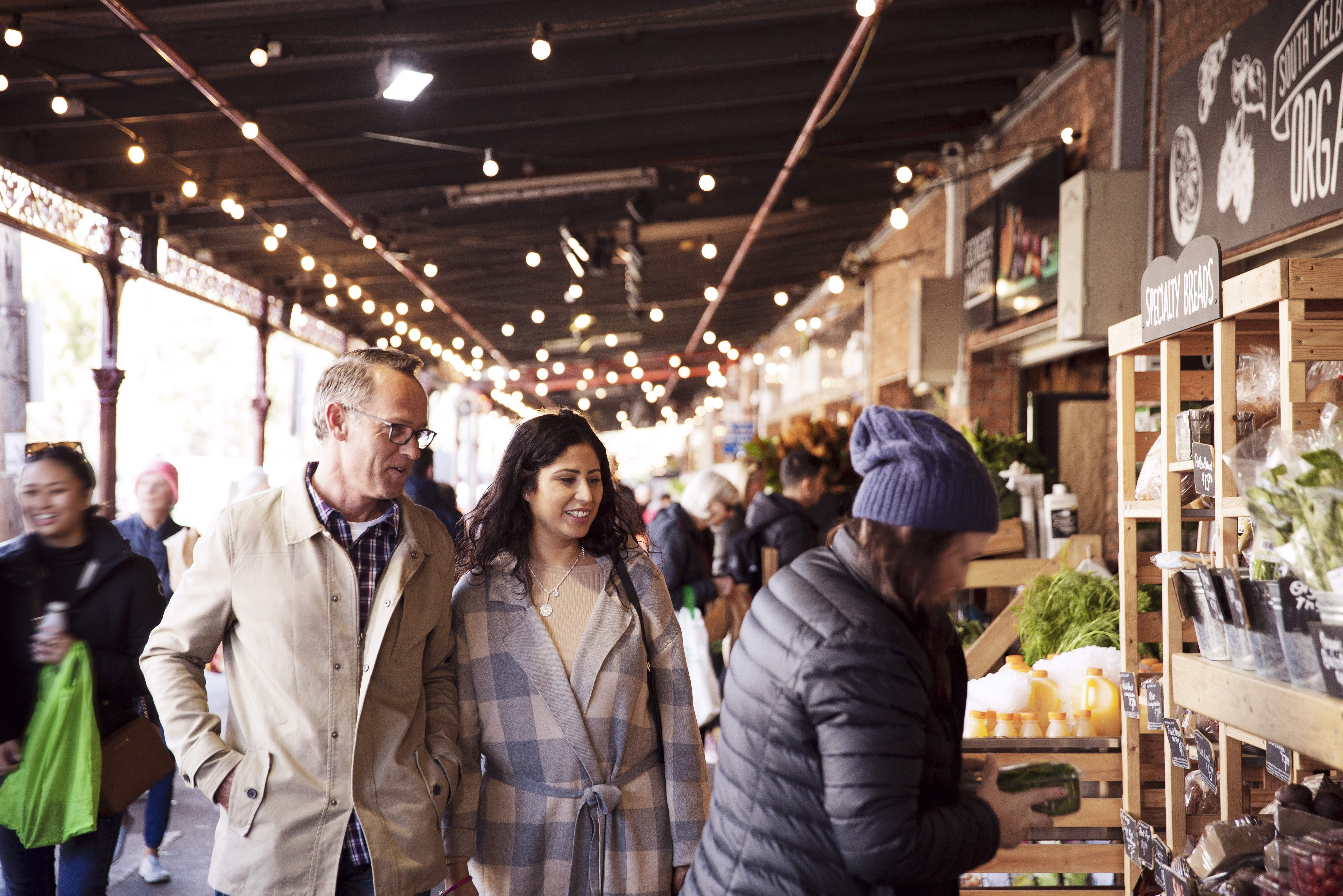 Focus is on two people walking down a buzzing isle at the South Melbourne Markets. 