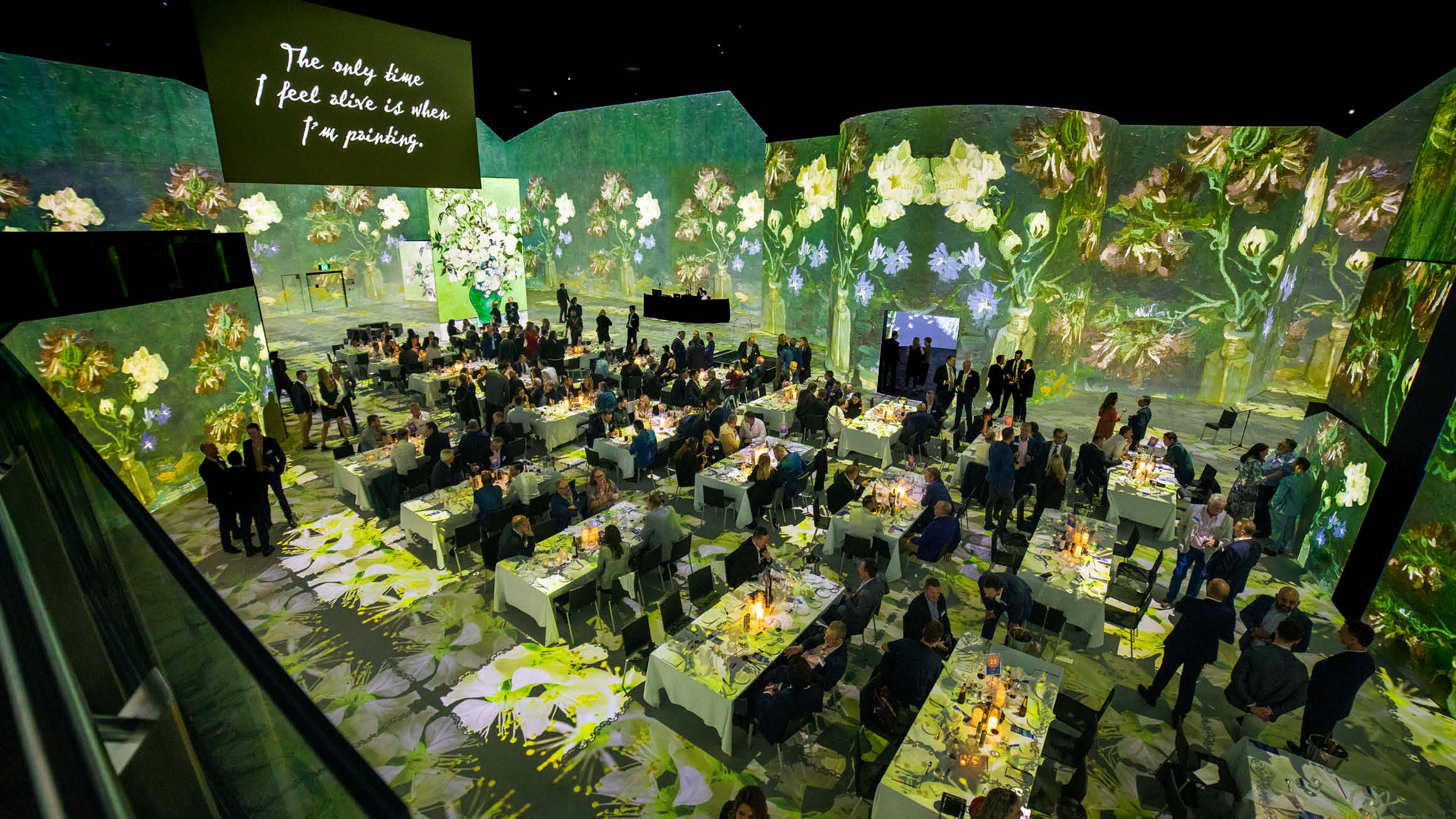 View from mezzanine level at THE LUME Melbourne, overlooking a formal gala dinner with rows of tables and people gathered around them talking. 