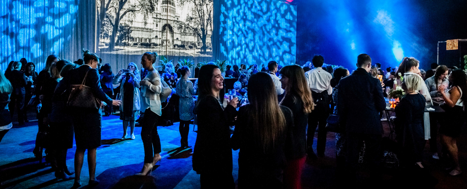 Crowd of people socialising with drinks under blue lights. 
