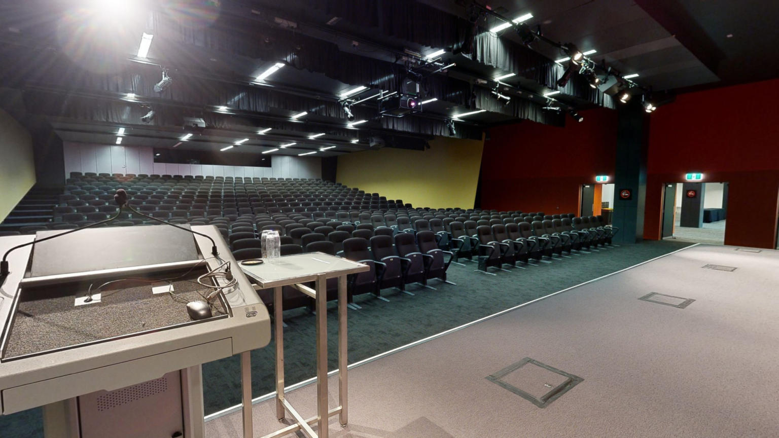 A spacious auditorium featuring neatly arranged rows of chairs and a prominent podium at the front, perfect for hosting large events and conferences.