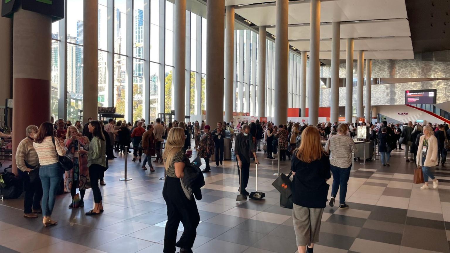 Large crowd of people standing or walking around the Convention Centre foyer at MCEC. 