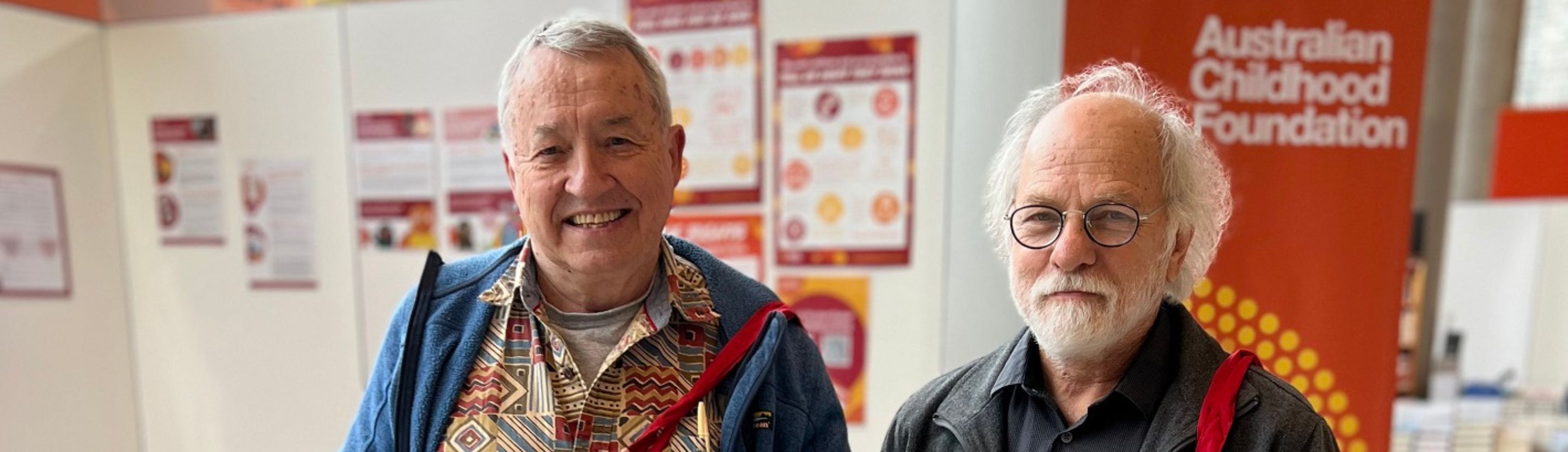 Two men smile at the camera with the Australian Childhood Foundation logo in the background. 