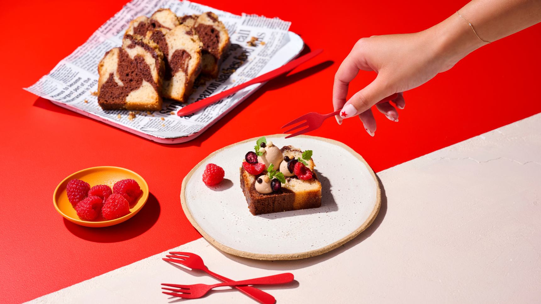 Event food: Chocolate, vanilla, and coffee marble cake on a white plate, beside an orange bowl of raspberries.