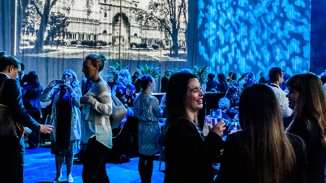 Crowd of people socialising with drinks in hand under blue lights. 