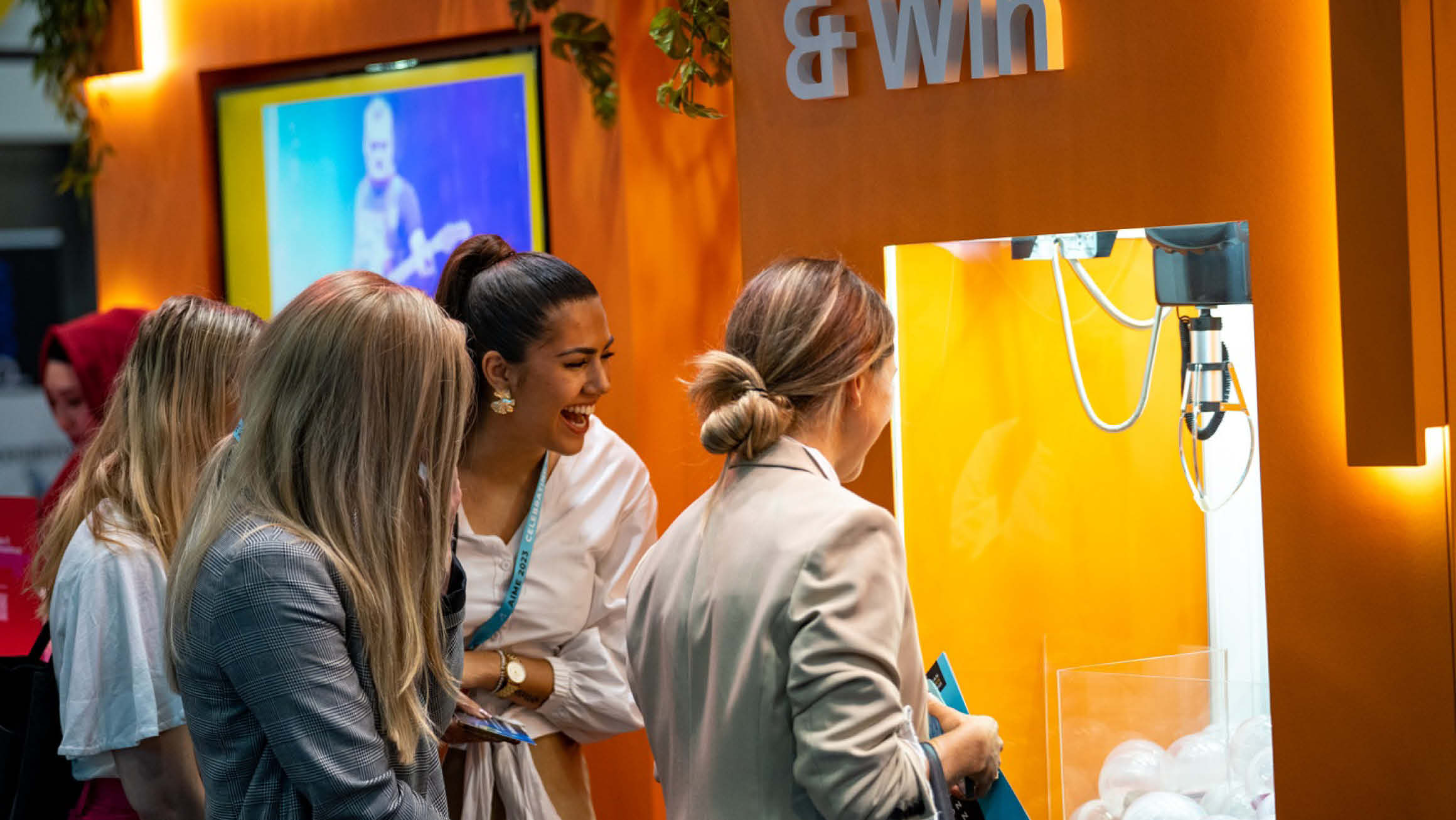 Four women gathered around an engaging orange claw machine game, with one woman actively playing while the others observe with anticipation.