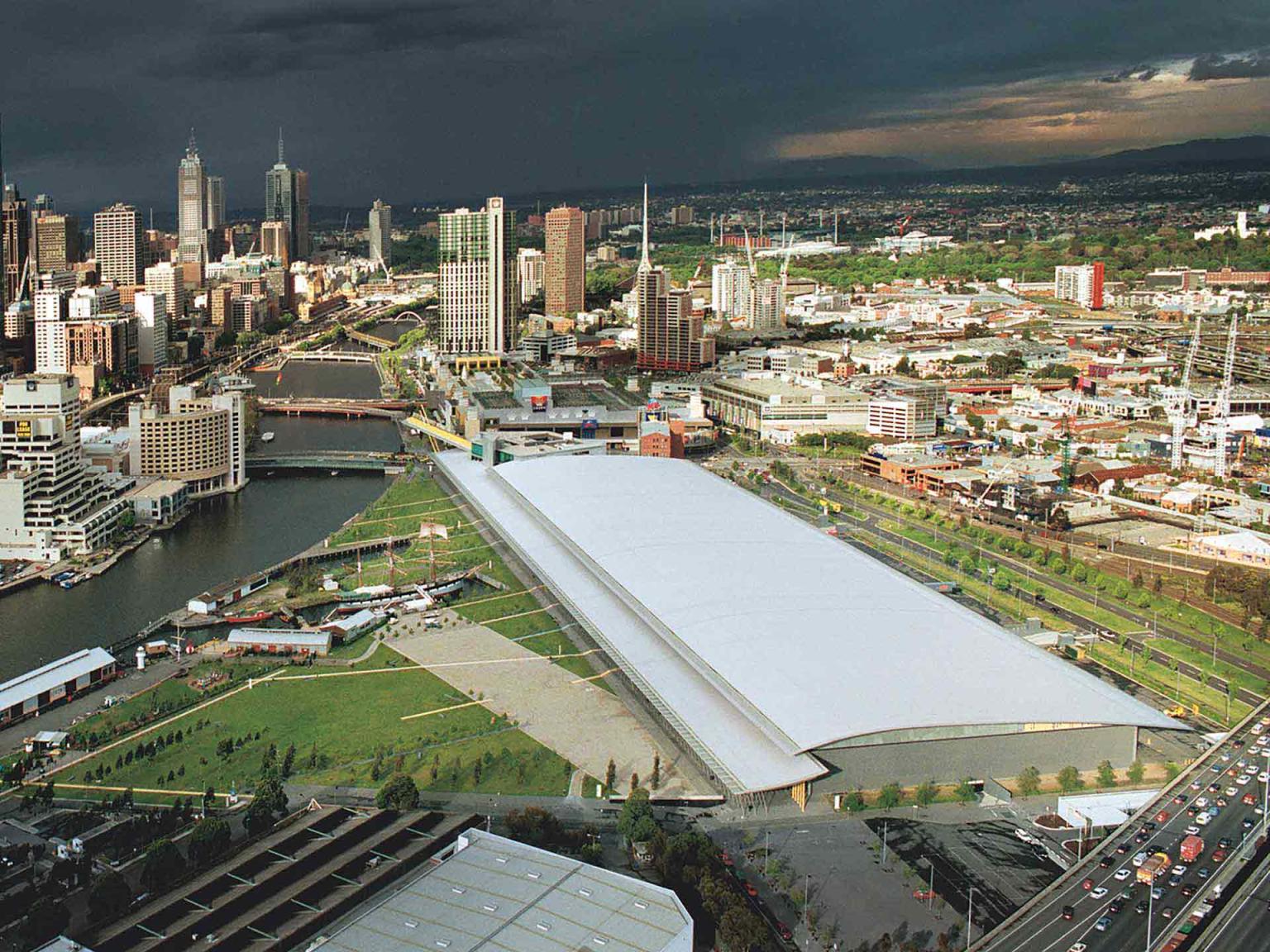 View from high in the sky of the Melbourne Exhibition building. The new convention centre can been seen in the bottom of the image under construction. Dark blue skies are on the horizon. 