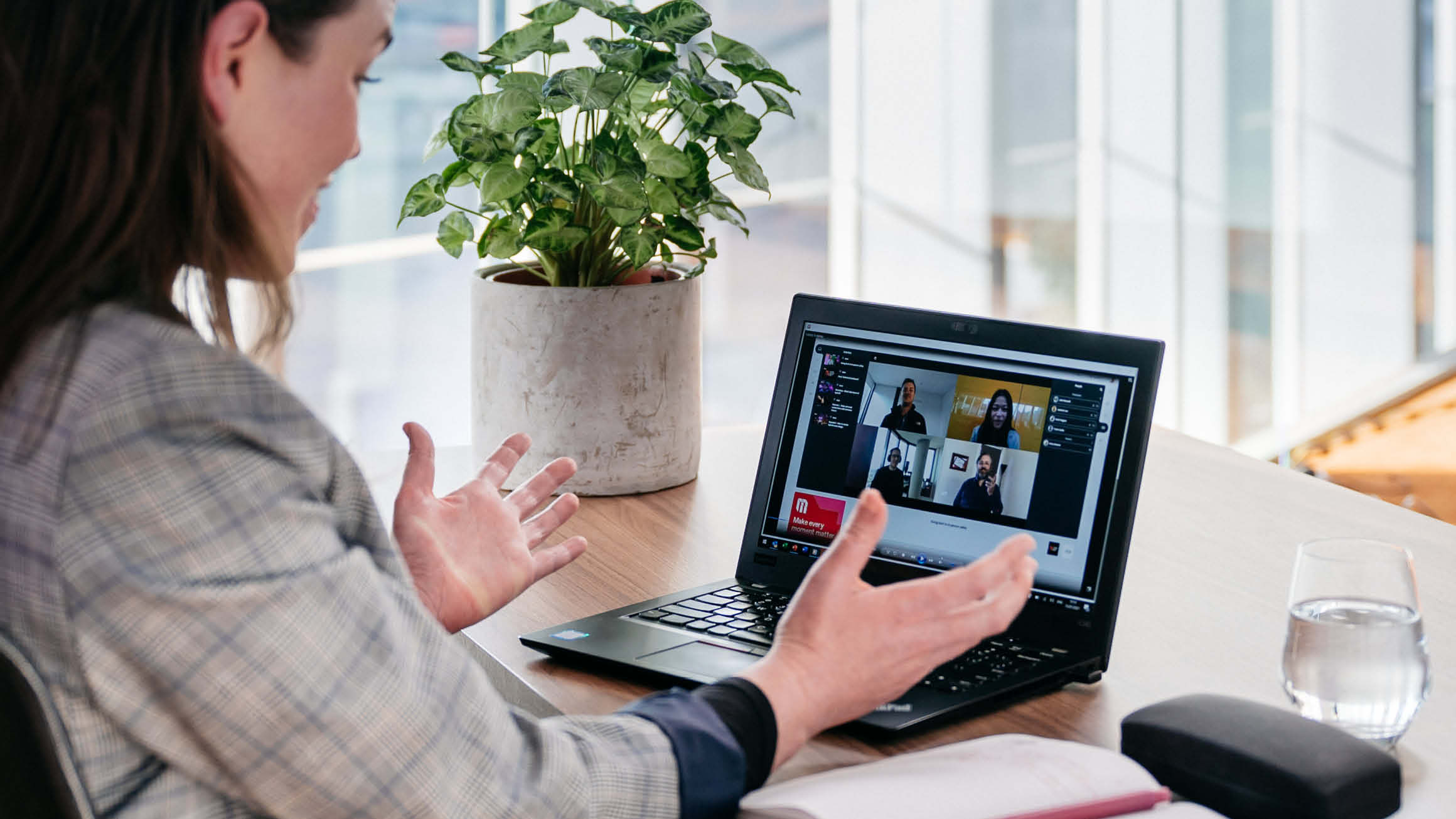 Women sitting at a desk looking at a computer that has a video conferencing call on screen with four people in view. 