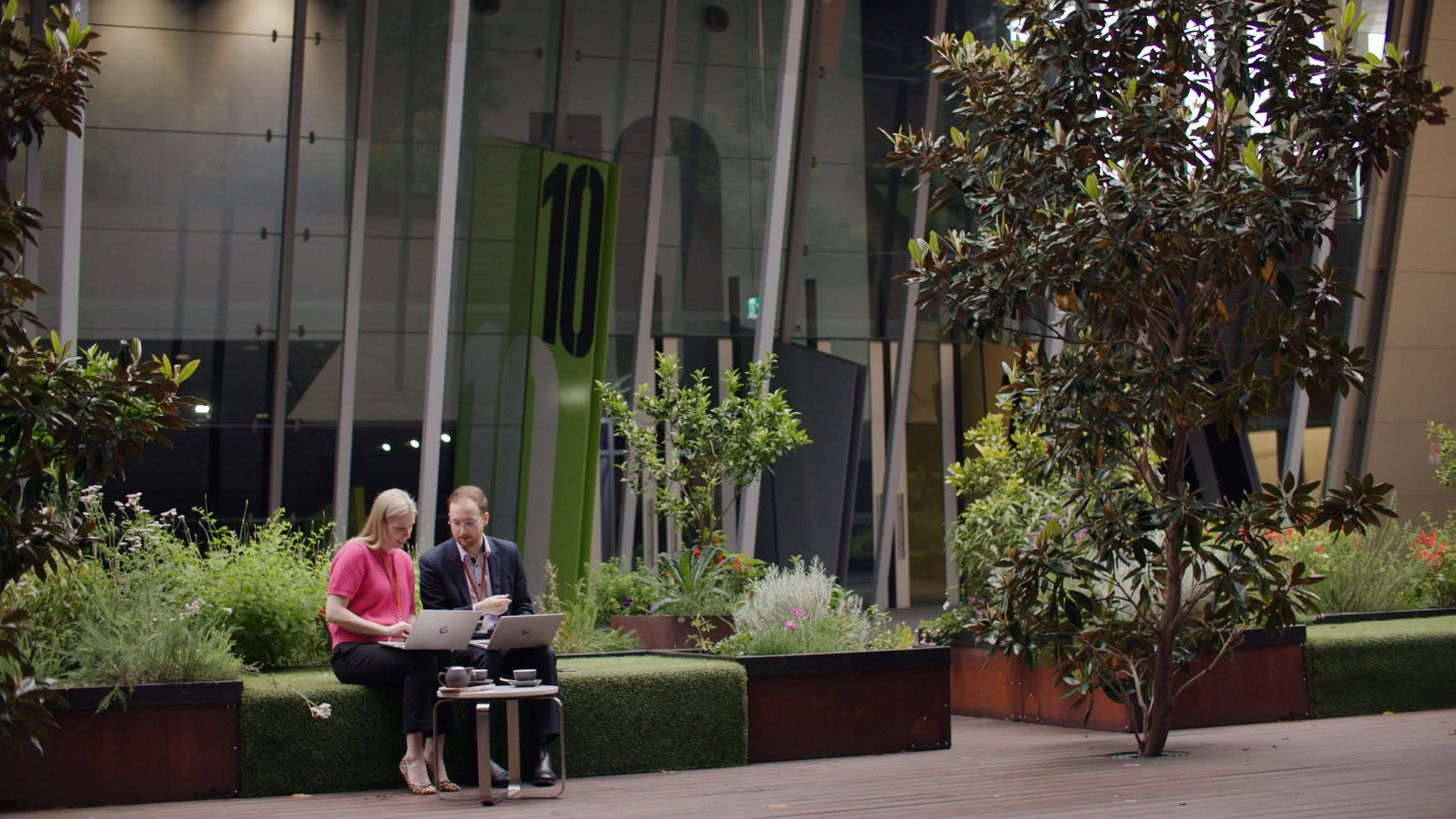 Anthea Fahey sitting outdoors with a man, both engaged in a conversation while looking at a laptop.