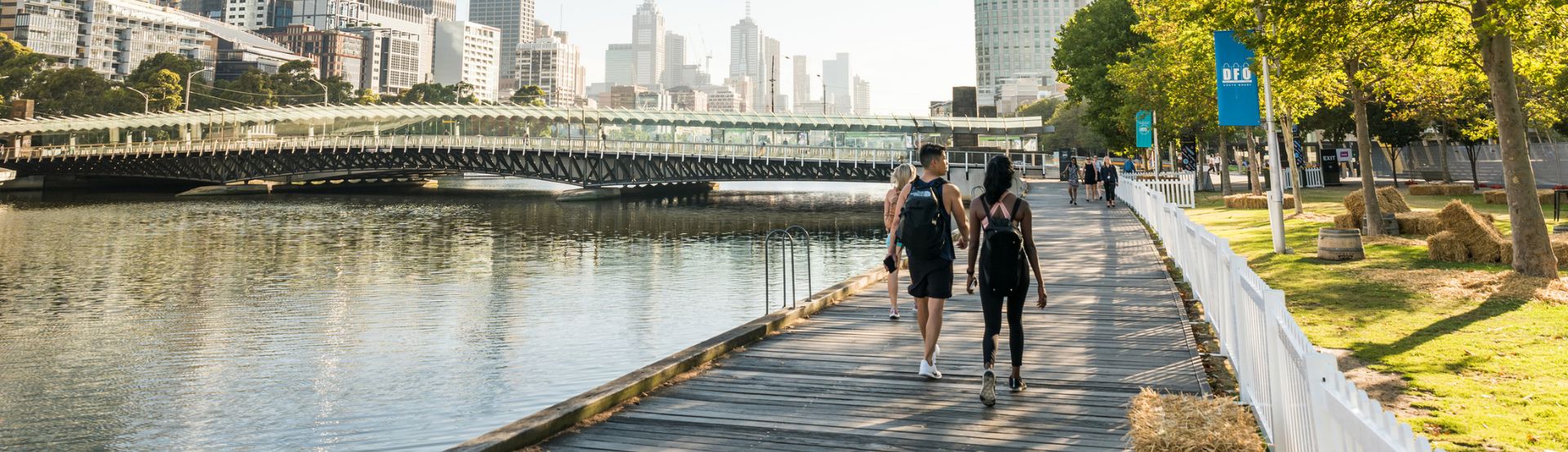 Two people walking on a board in Melbourne. Sun is shining on the river. 