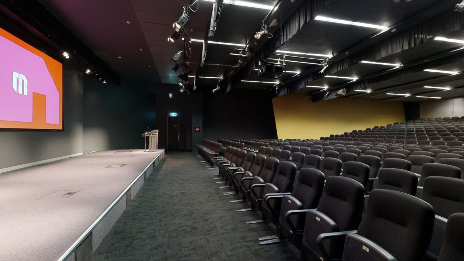 An expansive auditorium featuring multiple rows of seating and a prominent projector screen for presentations and events.