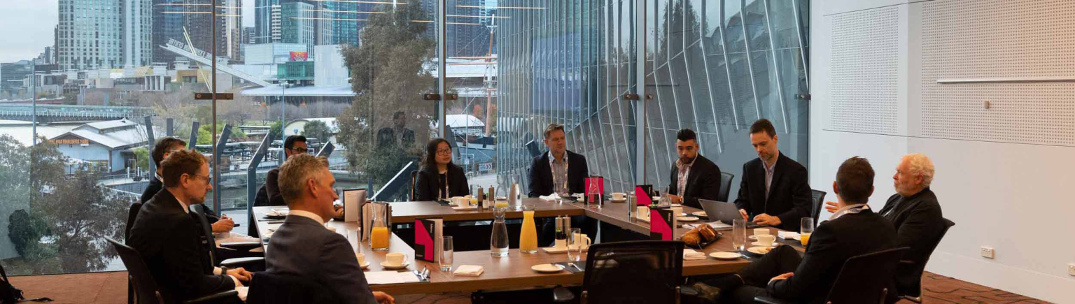 Melbourne meeting rooms: Professionals at a table with laptops, paperwork, and beverage, framed by a city view.