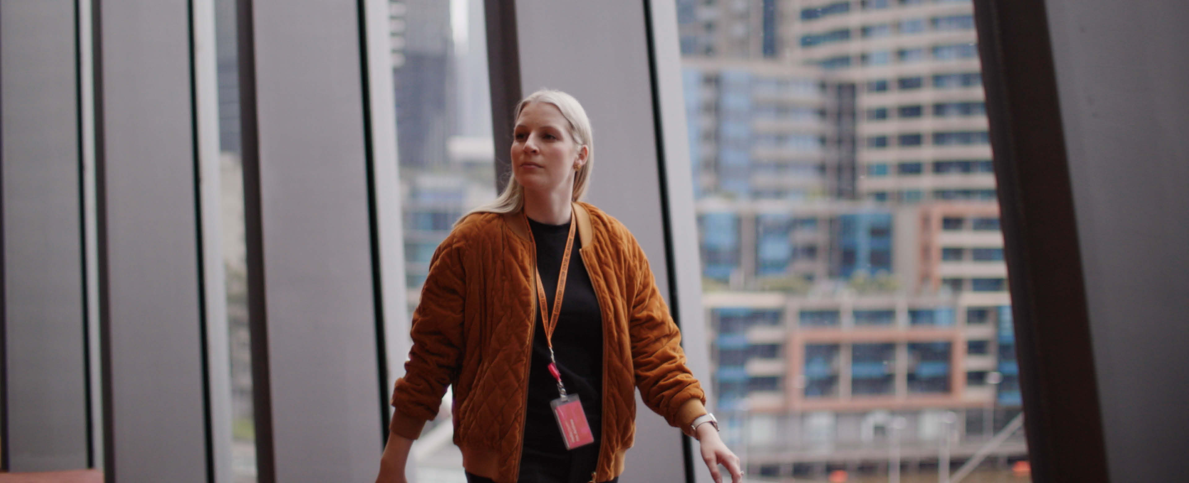 Anthea Fahey, a woman wearing an orange jacket is walking, looking off-camera.