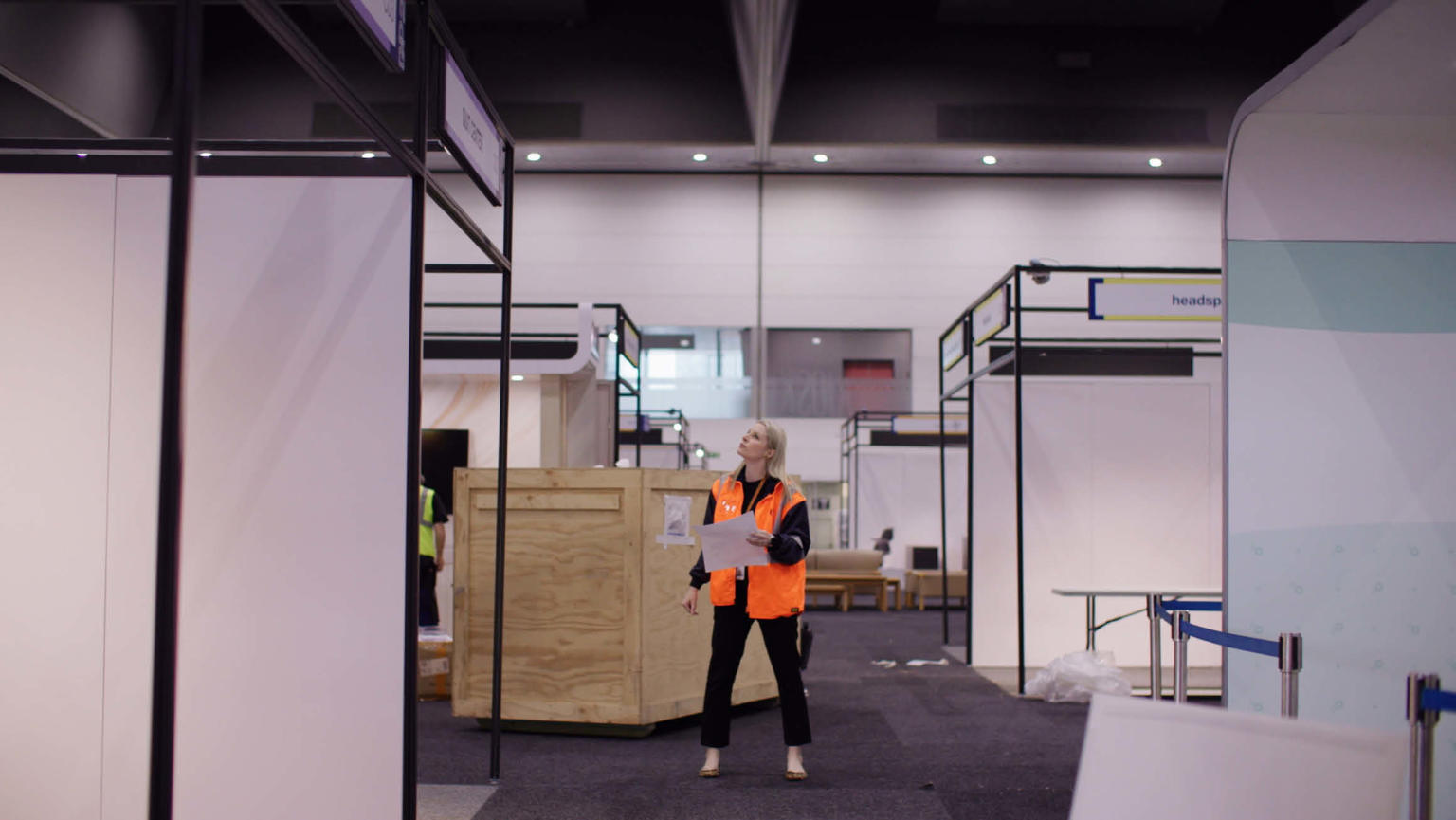 Anthea Fahey standing amidst an exhibition setup, wearing a high-visibility vest and a hard hat.