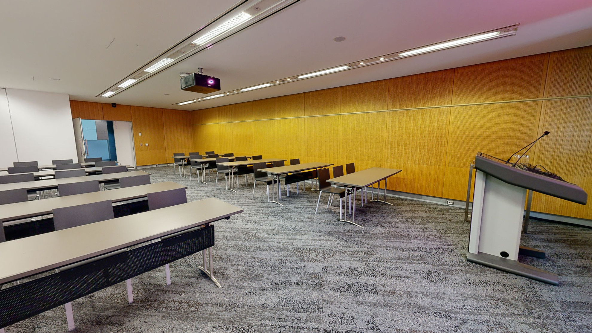 A meeting or conference room featuring neatly arranged tables and chairs in rows, providing a professional setting for meetings and discussions. A lectern sits at the front of the room. 