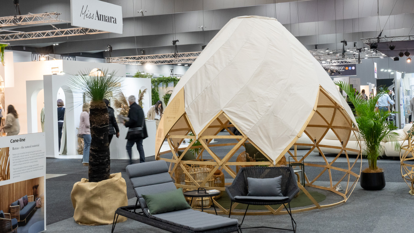 A wooden dome structure sits on display with a white fabric cover over the top. An exhibition of furniture surrounds the dome. 