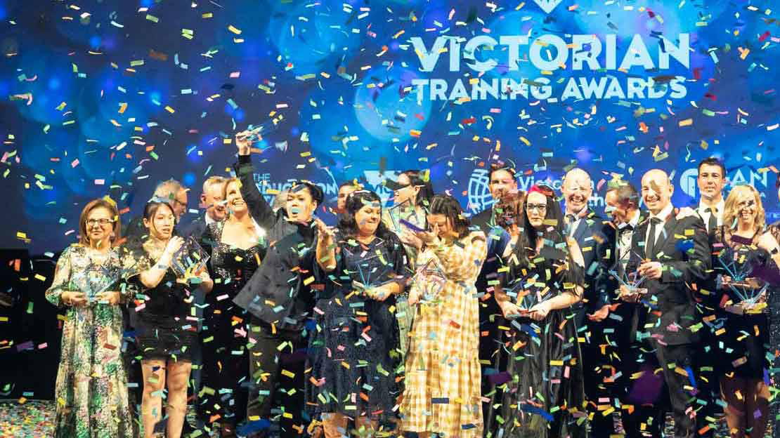 Crowd of people happily standing on a stage with colourful confetti falling down over them. 