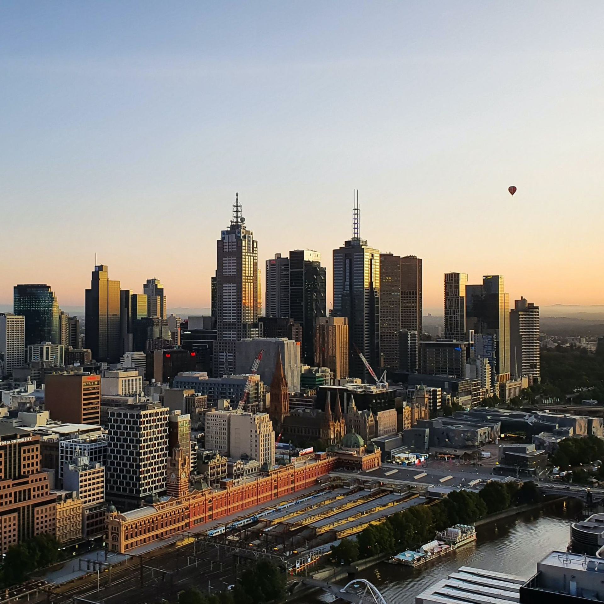 View from the sky of the city of Melbourne at sunrise. A lone air balloon floats in the sky in the distance. 