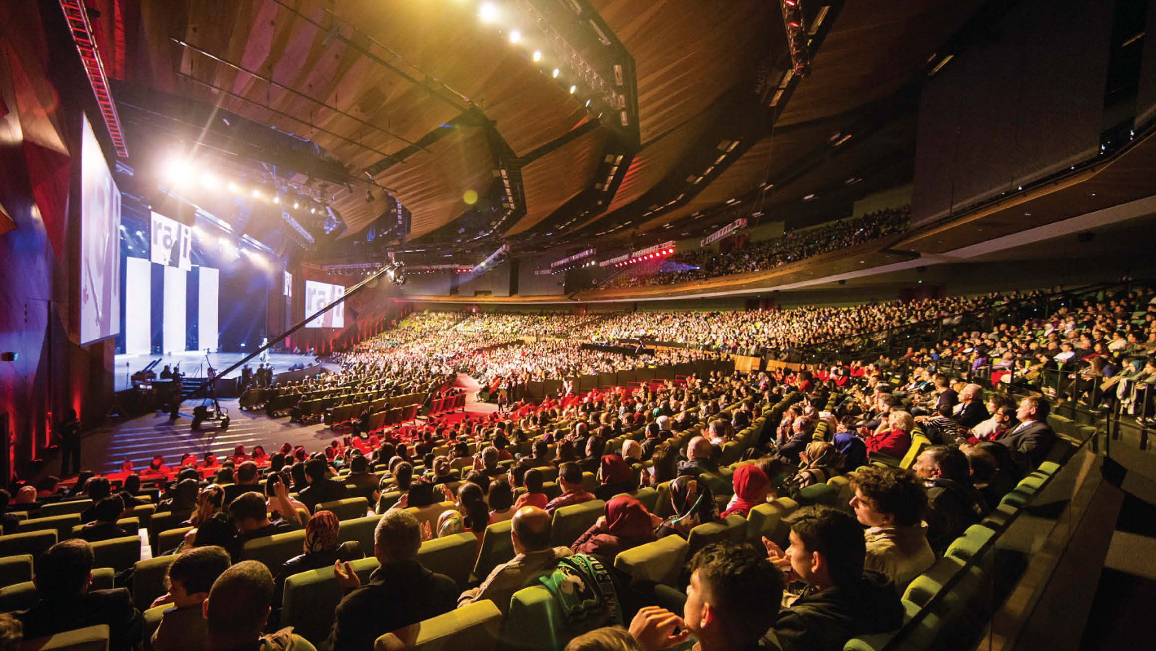 Plenary at MCEC (Melbourne Convention and Exhibition Centre) is filled with people looking at the stage with is light up for a presentation. 