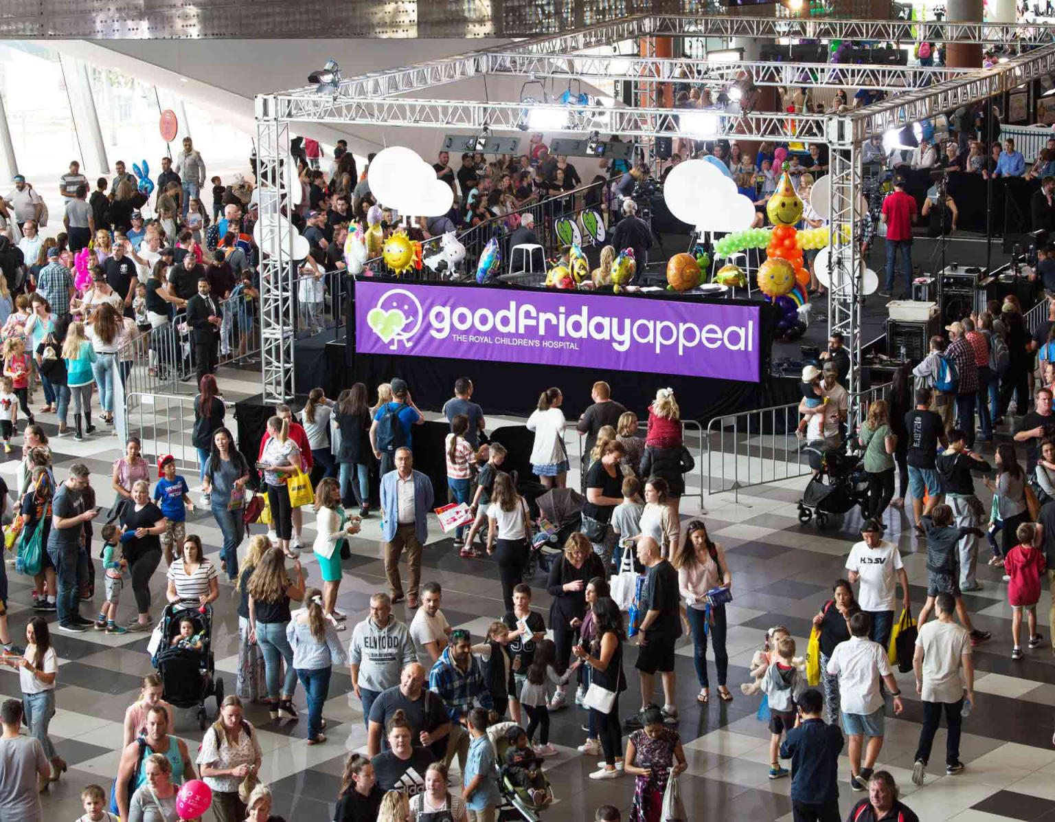 Crowd of people walking around foyer with a Good Friday Appeal purple sign in the centre. 