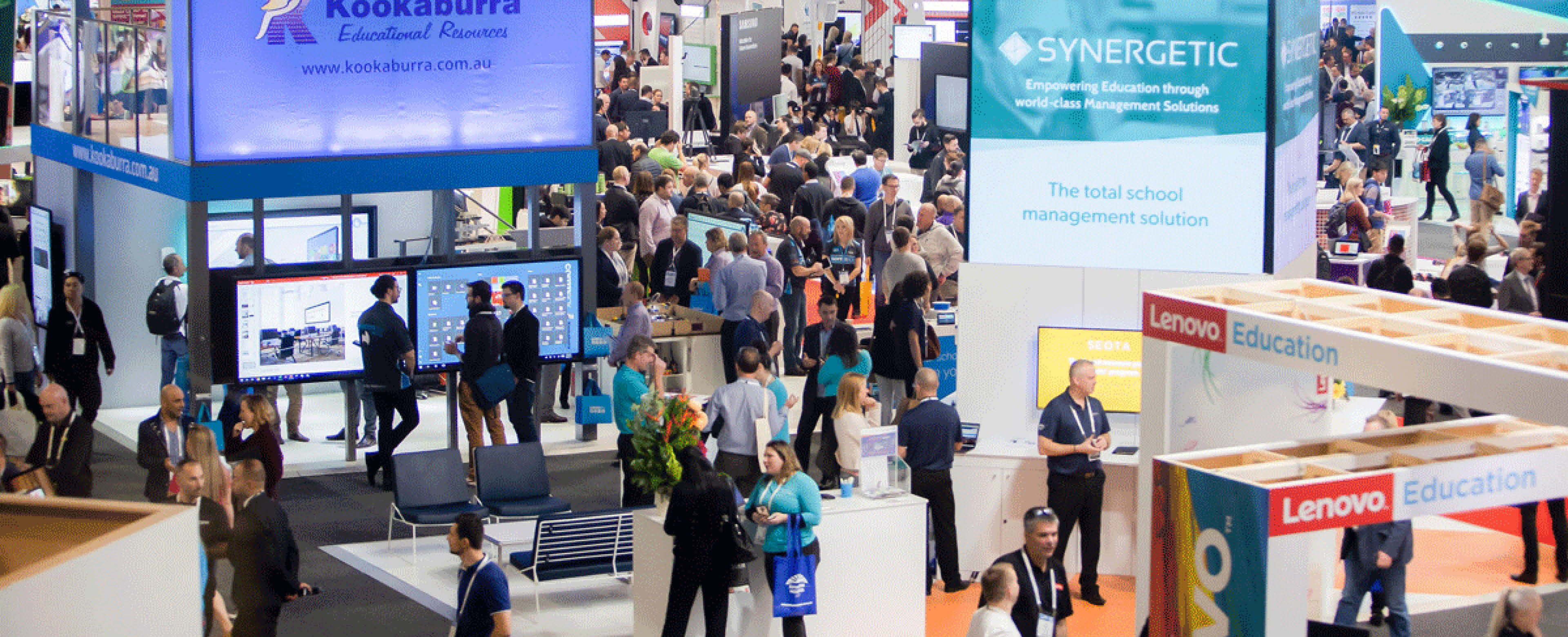 Over head view of an exhibition event with lots of people walking around exhibition booths. 