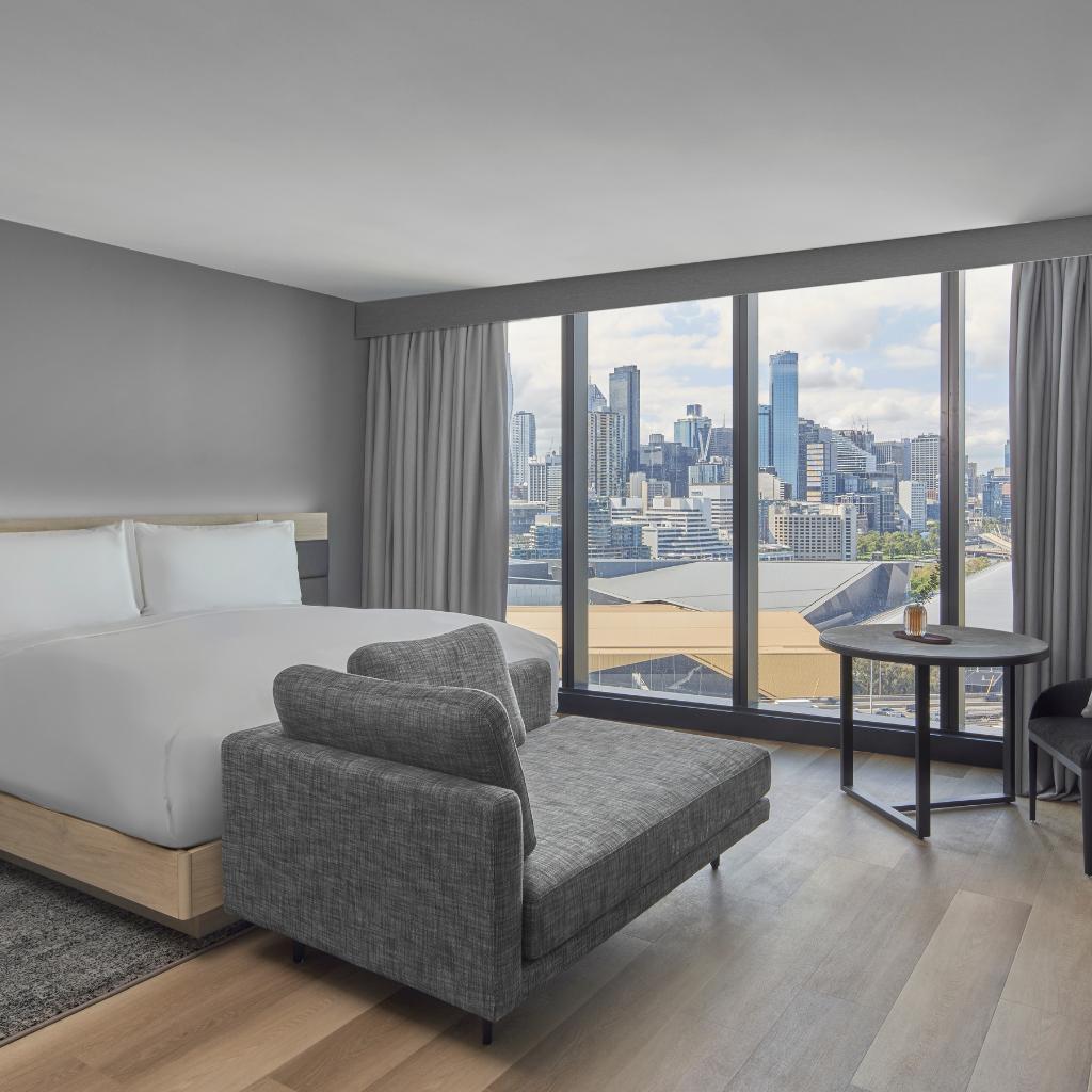 Inside a hotel room with a queen bed and a lounge at the foot of the bed.