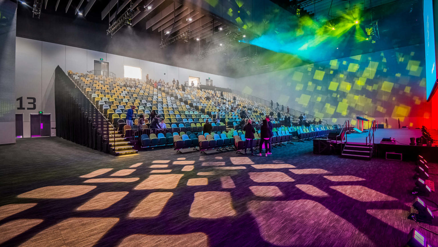 A vibrant auditorium with tiered seating overlooking a well-lit stage, adorned with captivating colourful lights.