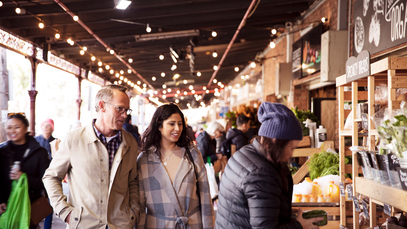 Focus is on two people walking down a buzzing isle at the South Melbourne Markets. 