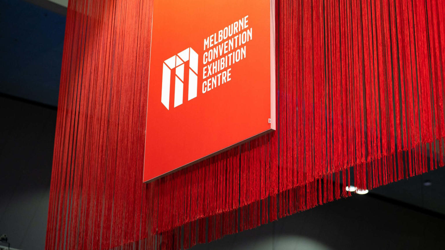 Striking long red fringing accompanied by a prominent red board displaying a logo and the text 'Melbourne Convention Exhibition Centre'.