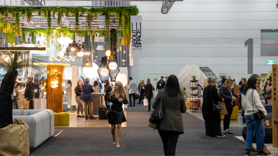 Crowd of people stroll through an exhibition of furniture and lighting displays. 