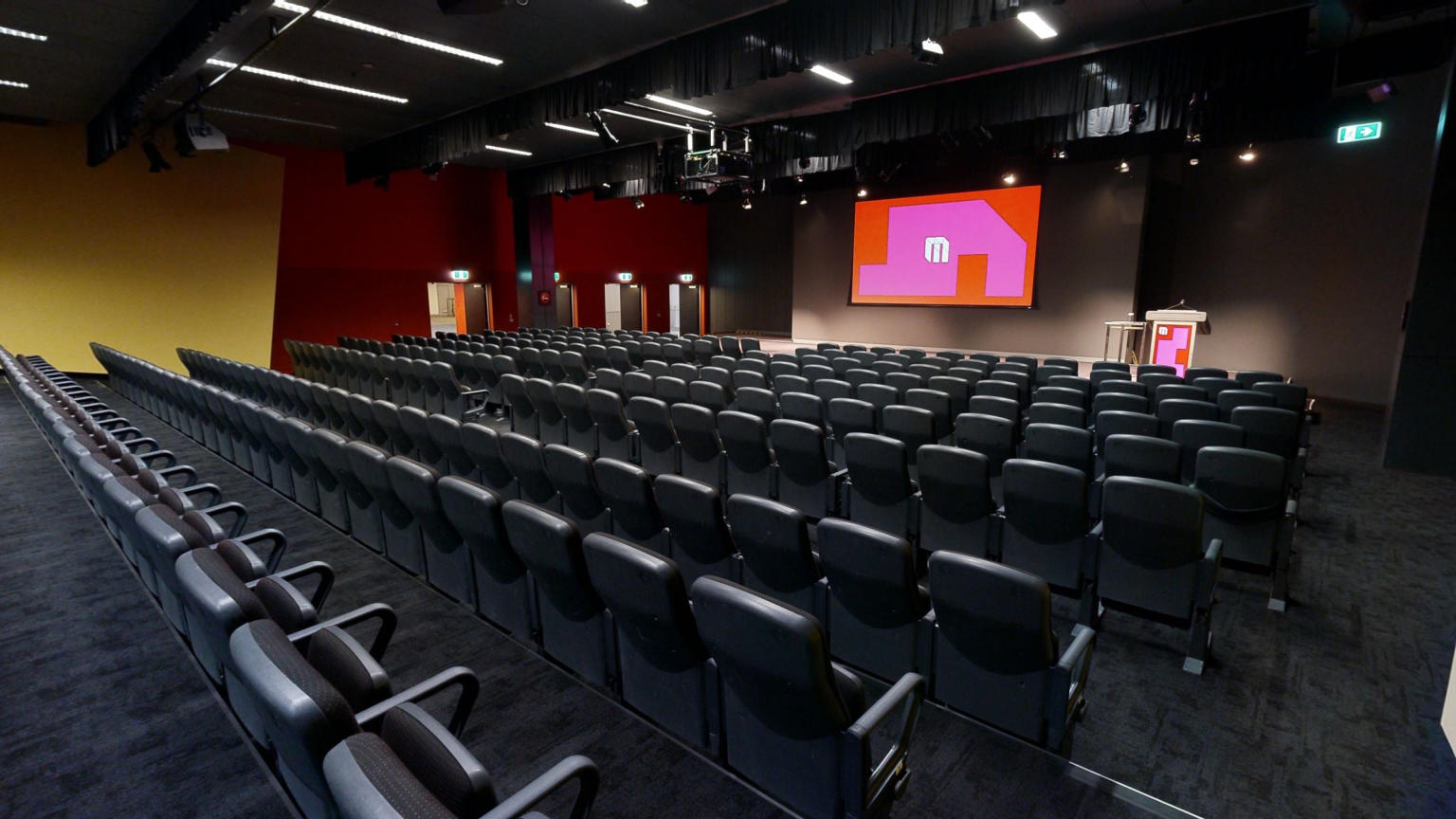 An expansive auditorium featuring multiple rows of seating and a prominent projector screen for presentations and events.