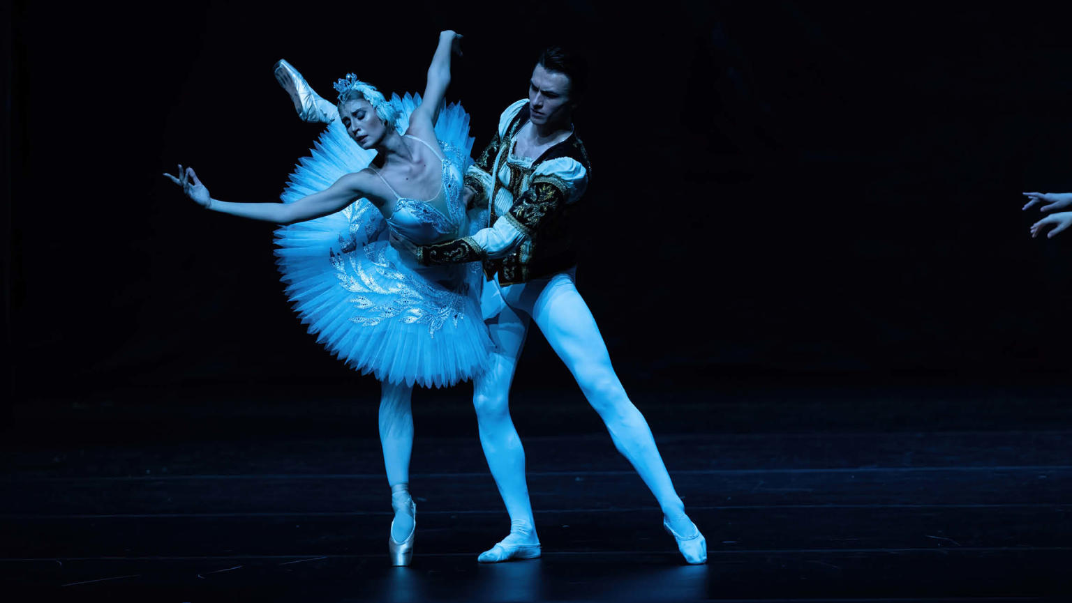 An image capturing a female ballerina in a tutu as she gracefully dances alongside a male danseur on a stage. 