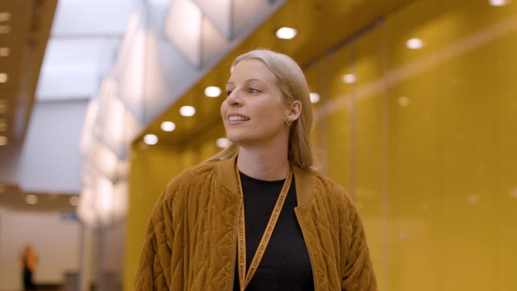 Anthea Fahey, a woman wearing an orange jacket, smiling and looking off-camera.