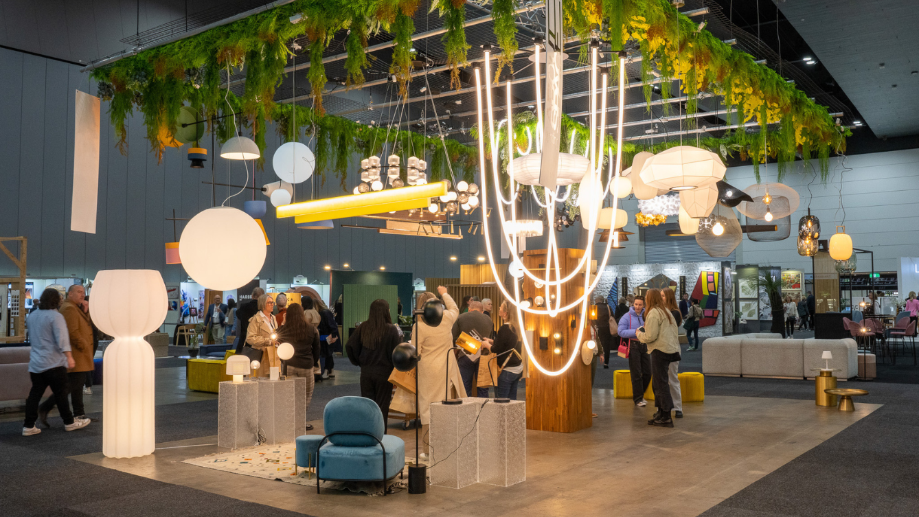 Light display with green foliage around it hangs over a rectangle display of various floor and table lamps. 