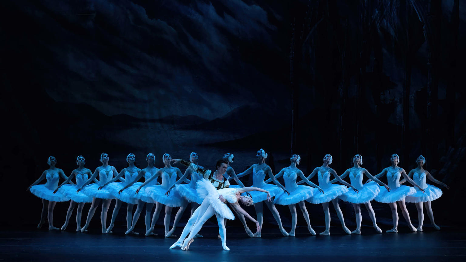 An image showcasing a dynamic composition: in the background, a group of ballerinas dances gracefully in a line, while in the foreground, a male danseur and a female ballerina captivate the viewer with their duet.