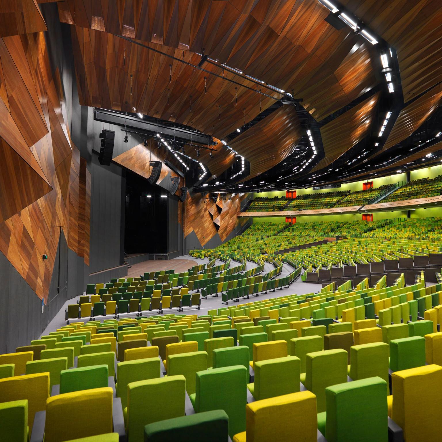 Side view of stage in a large plenary theatre. The rows of seats are made up of different shades of green and yellow.