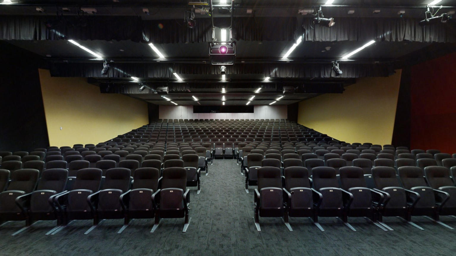 An expansive auditorium featuring multiple rows of seating and a prominent projector screen for presentations and events.