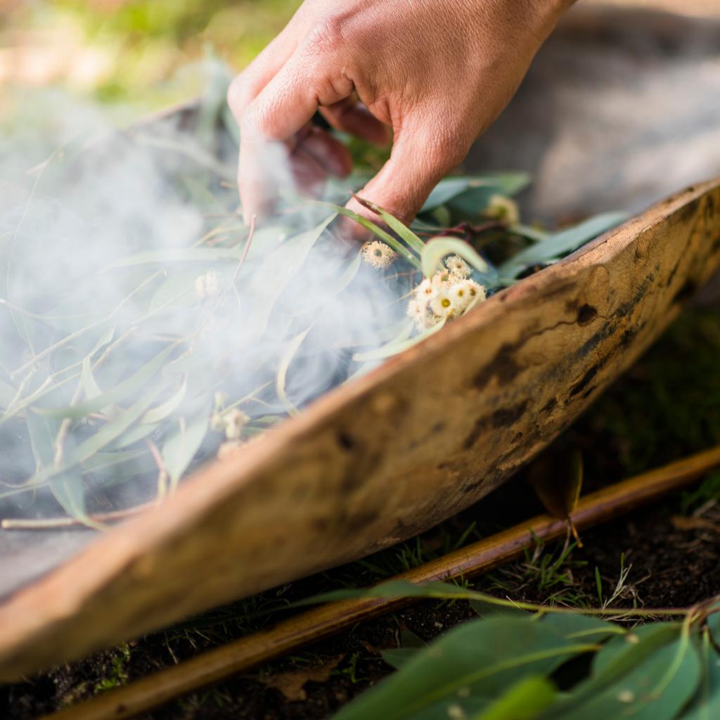 Close up of a Smoking Ceremony by First Nations People. A hand holding a collection of leaves in a wooden ball with smoke rising from it. 