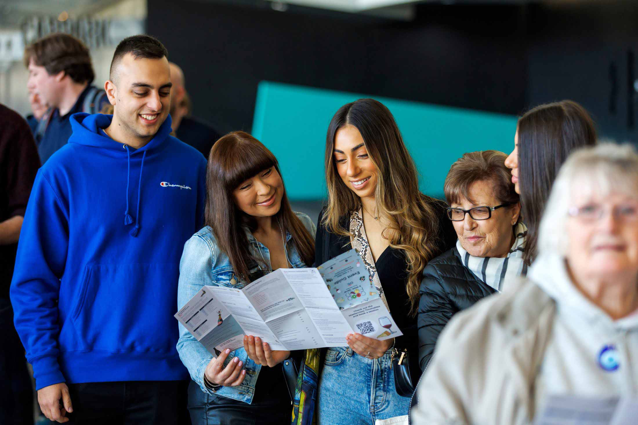 Group of people standing looking together at a unfolded large piece of paper. 