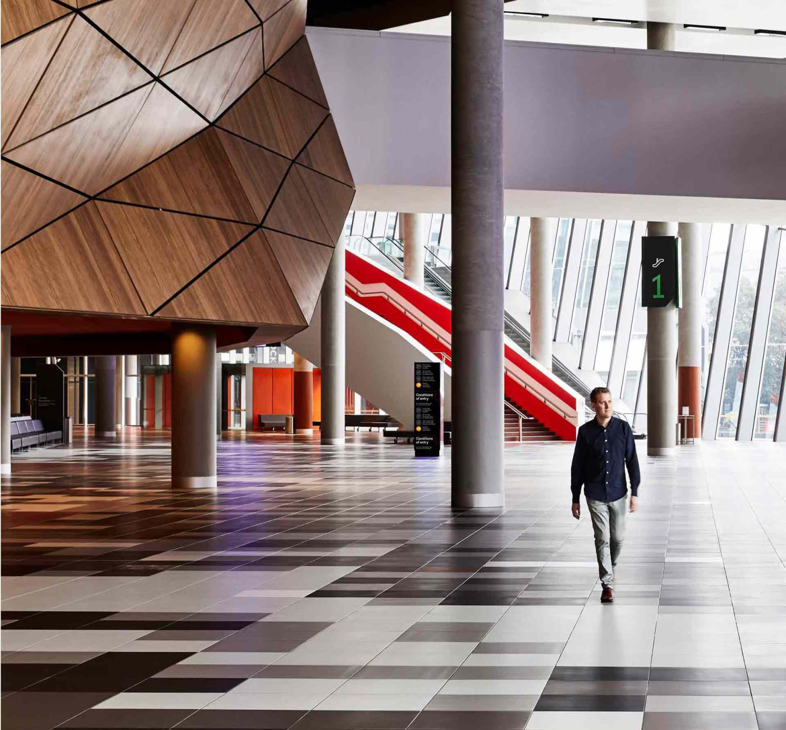 A man walking through an empty foyer with black and white tiles on the floor of the Melbourne Convention Centre.