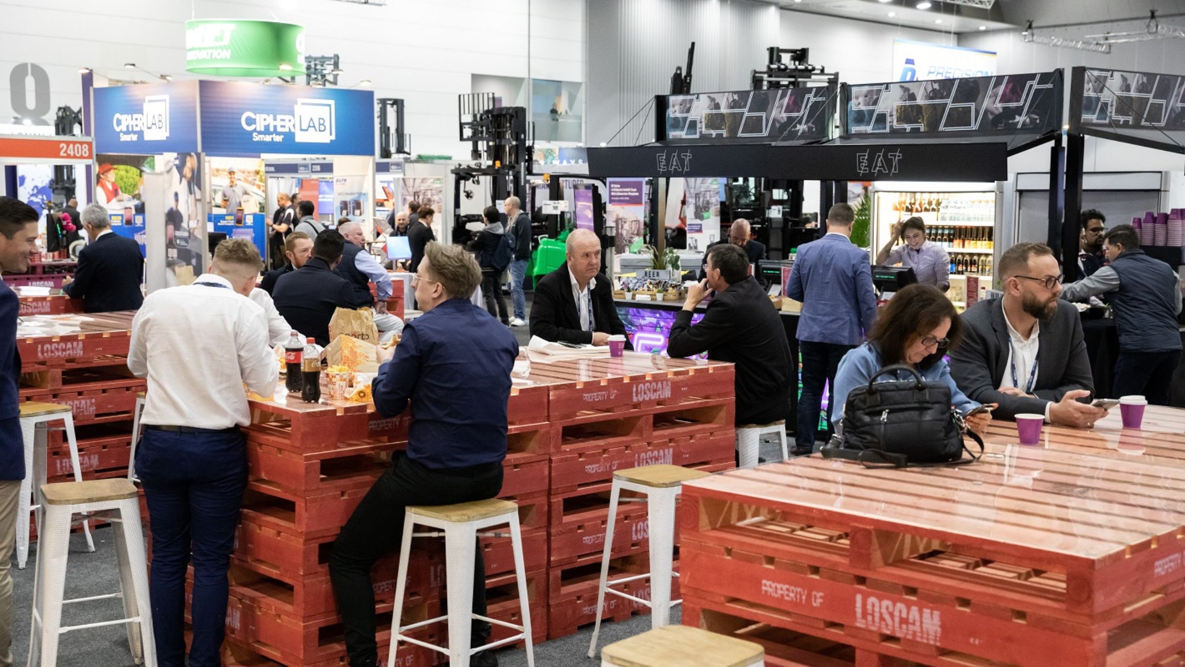 People sitting at tables made of wooden pallets at the Megatrans expo at MCEC. 