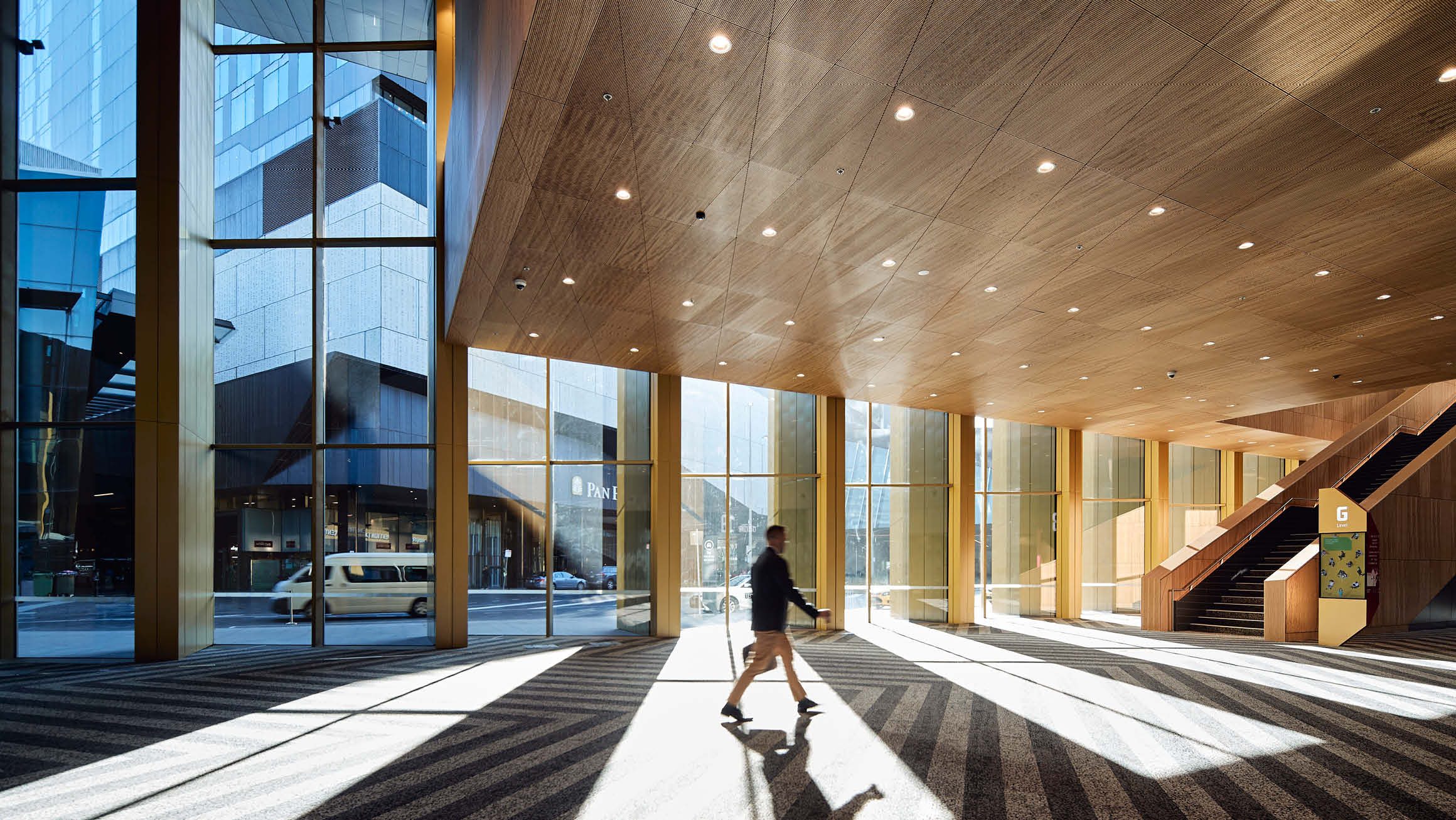 Man walking across open foyer at MCEC (Melbourne Convention and Exhibition Centre) with lots of natural light streaming in through the large windows. 