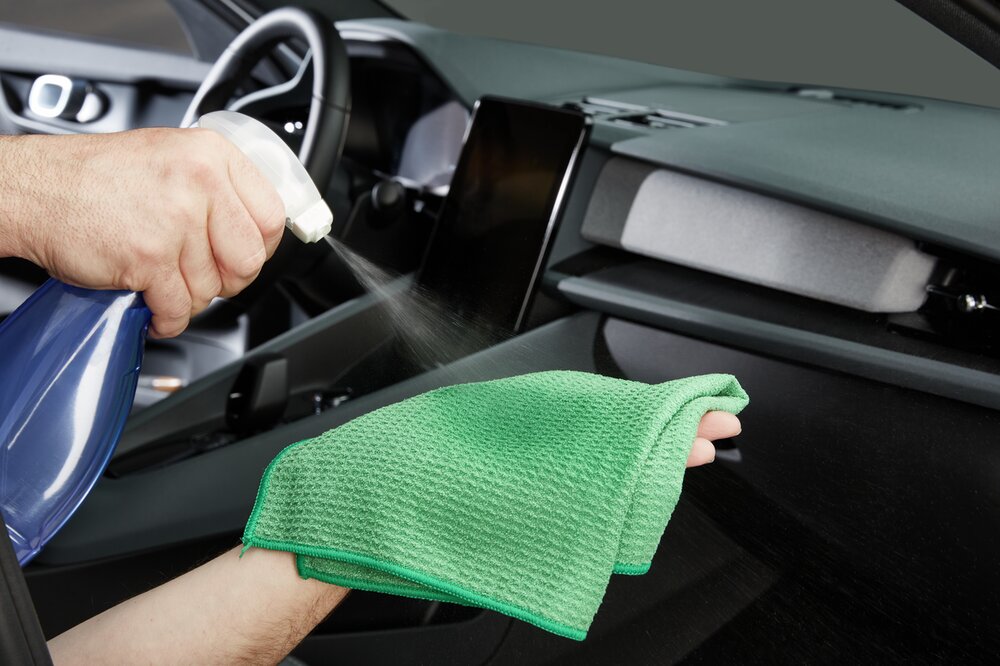 Jemand sprüht Autoinnenraumreiniger auf ein grünes Mikrofasertuch.