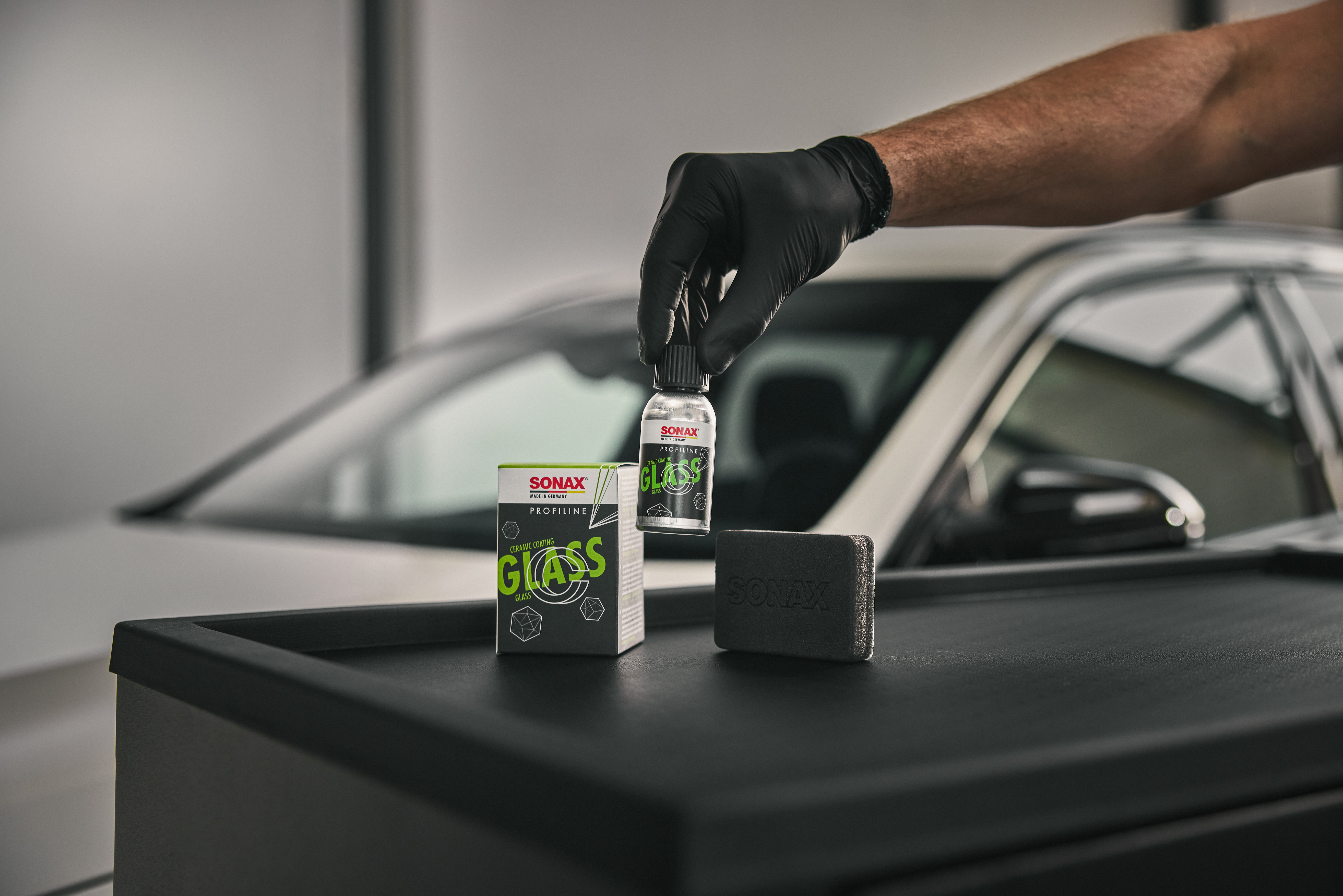Das CC Glass Produkt steht vor einem silbernen Auto.